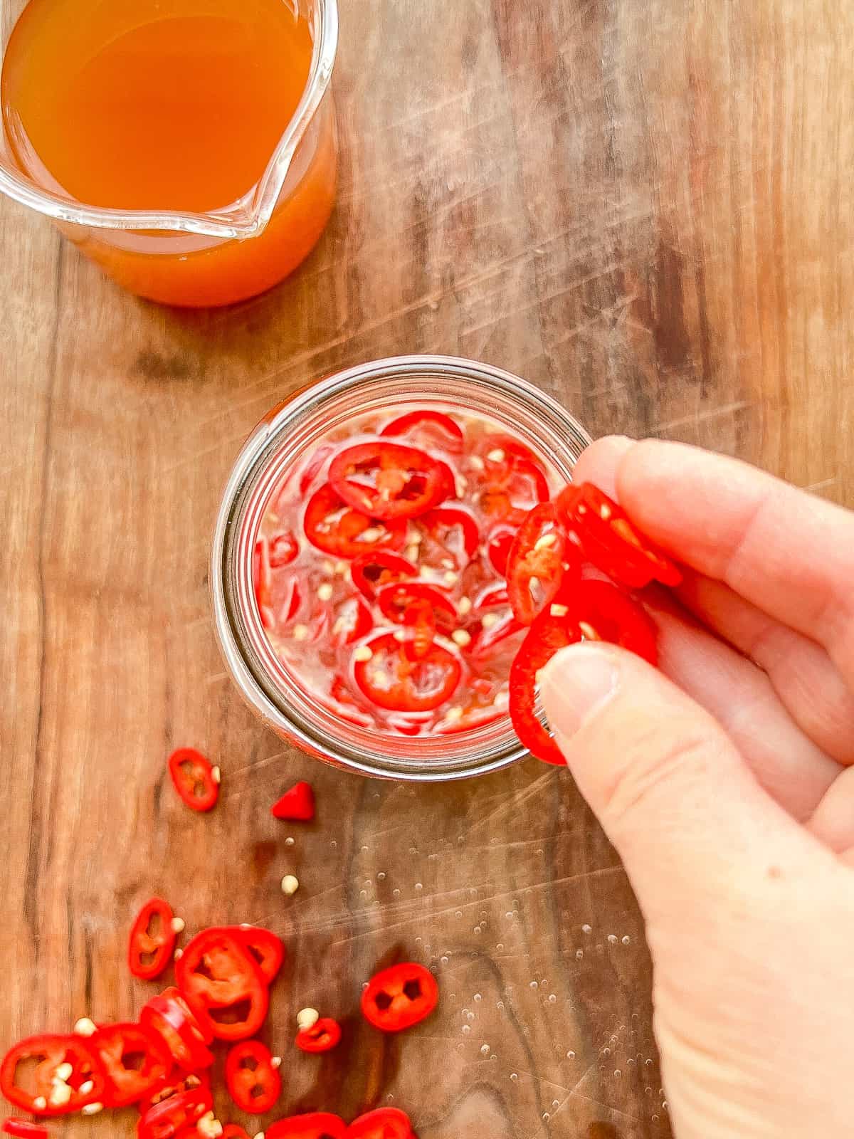 An image of a hand dropping sliced hot chillies into brine.