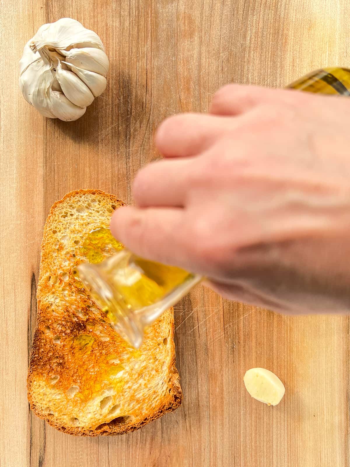 olive oil being poured over a slice of garlic toast