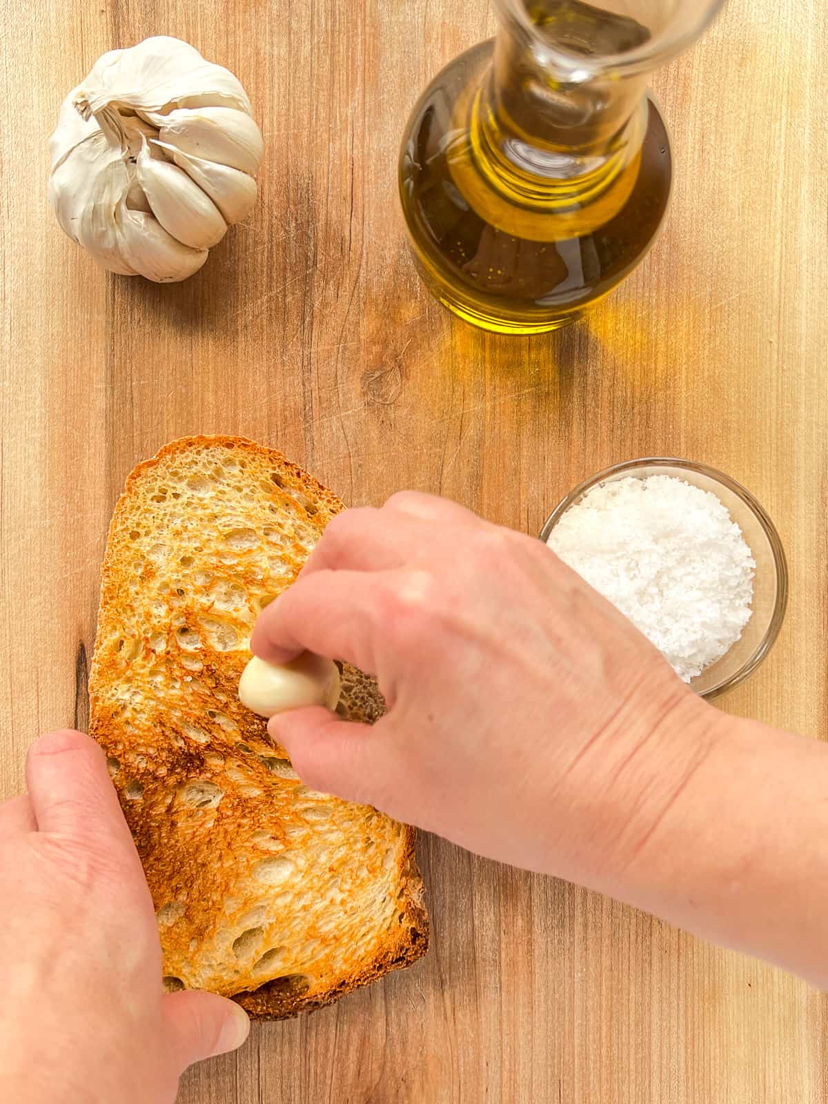 a garlic clove being rubbed over a slice of hot toast