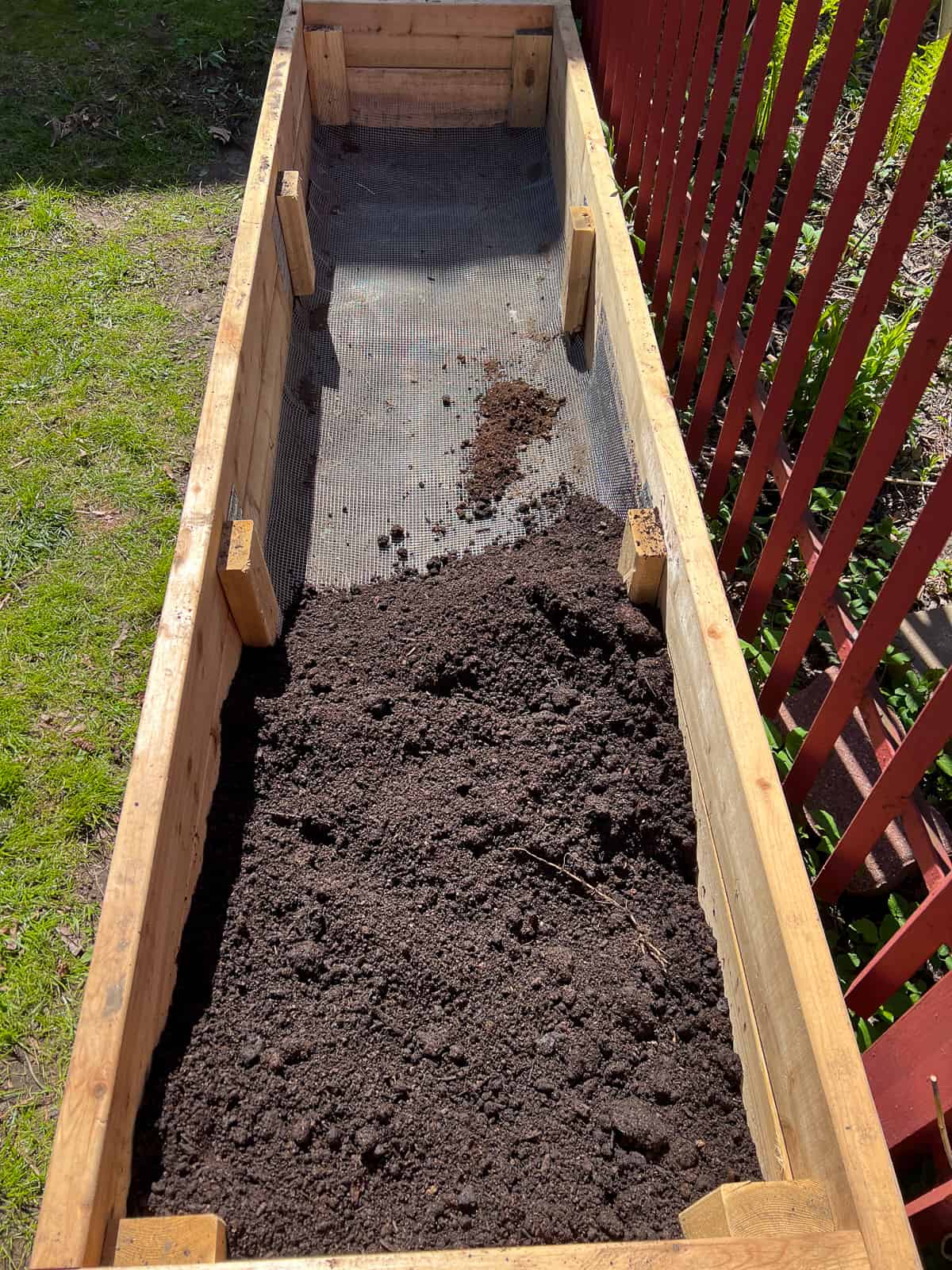 An image of a garden bed lined in metal mesh, beginning to be filled with soil, to help with the process of critter proofing raised bed.