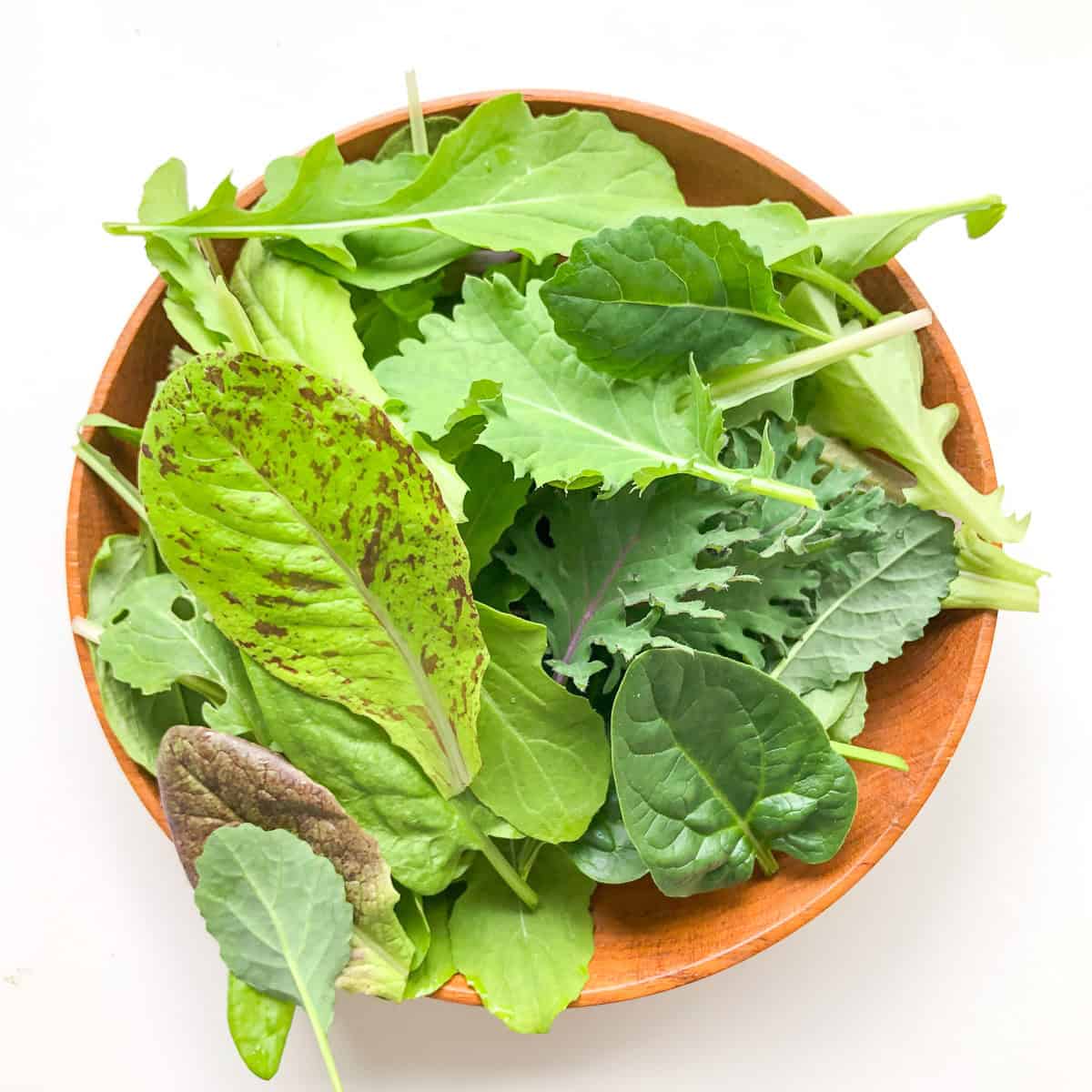 A wooden bowl containing salad greens.
