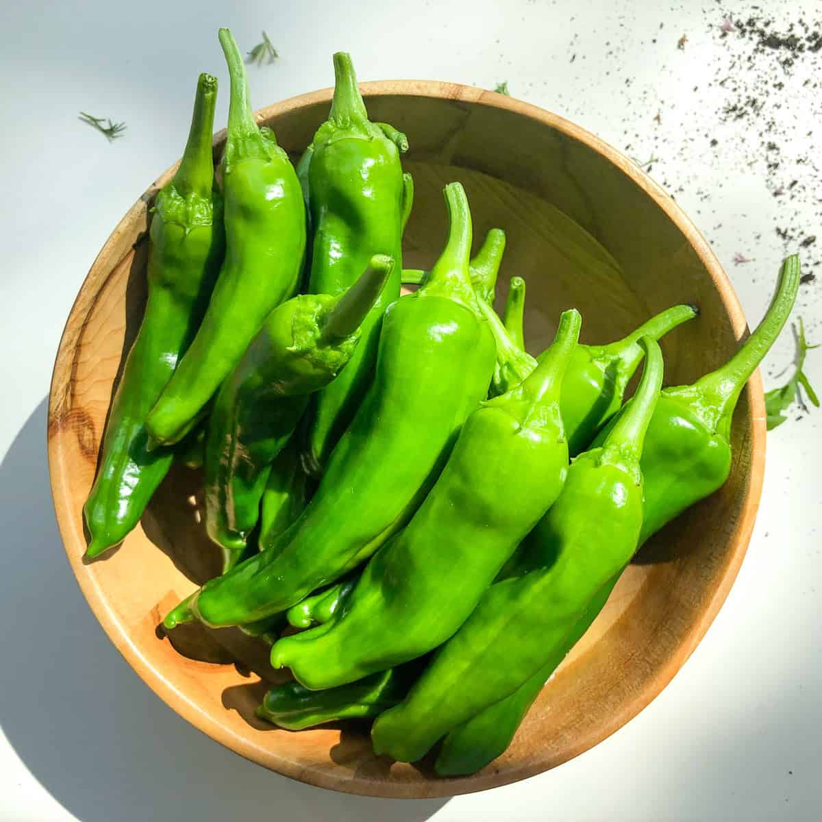 A wooden bowl containing shishito peppers.