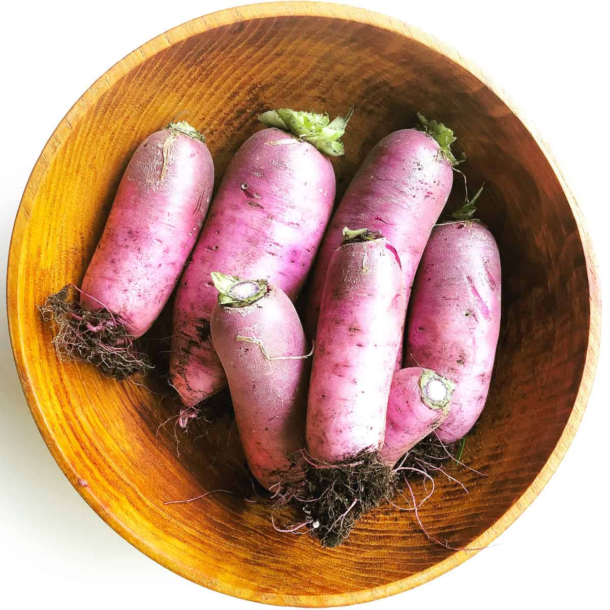 A wooden bowl containing mini purple daikon radishes.