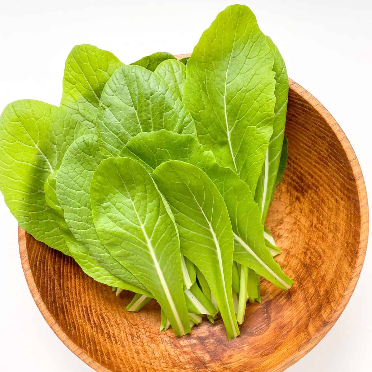 A wooden bowl containing mustard greens.
