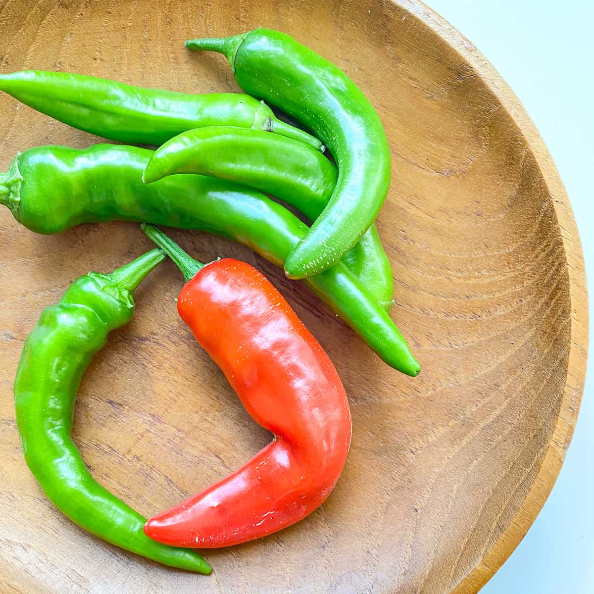 A bowl filled with green and red hot peppers.