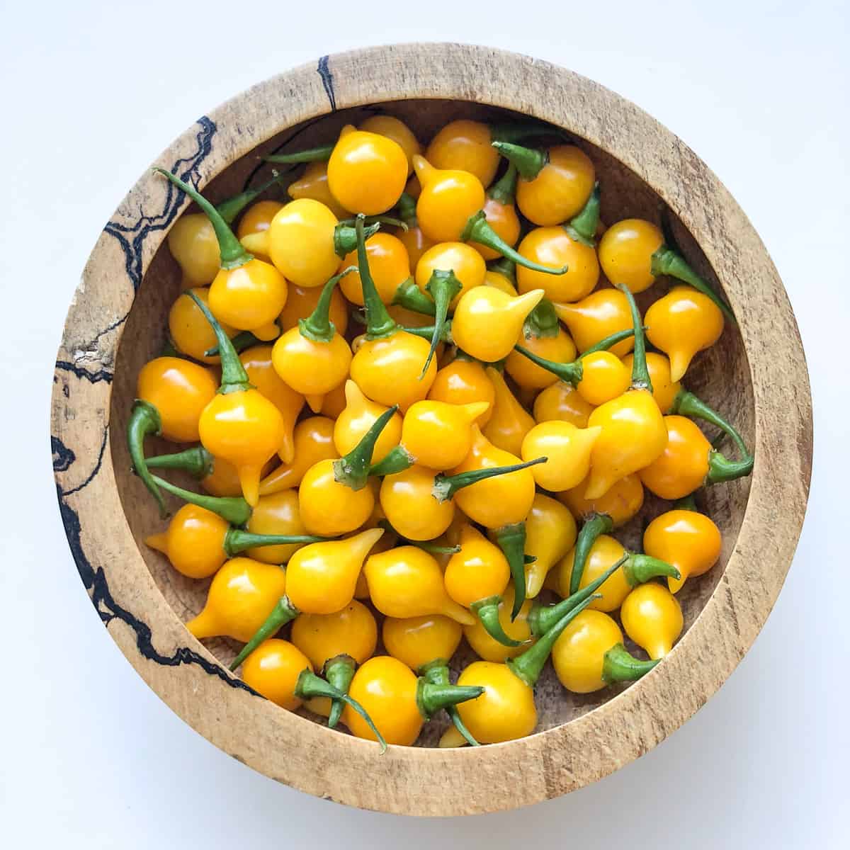 A bowl filled with small yellow hot peppers.