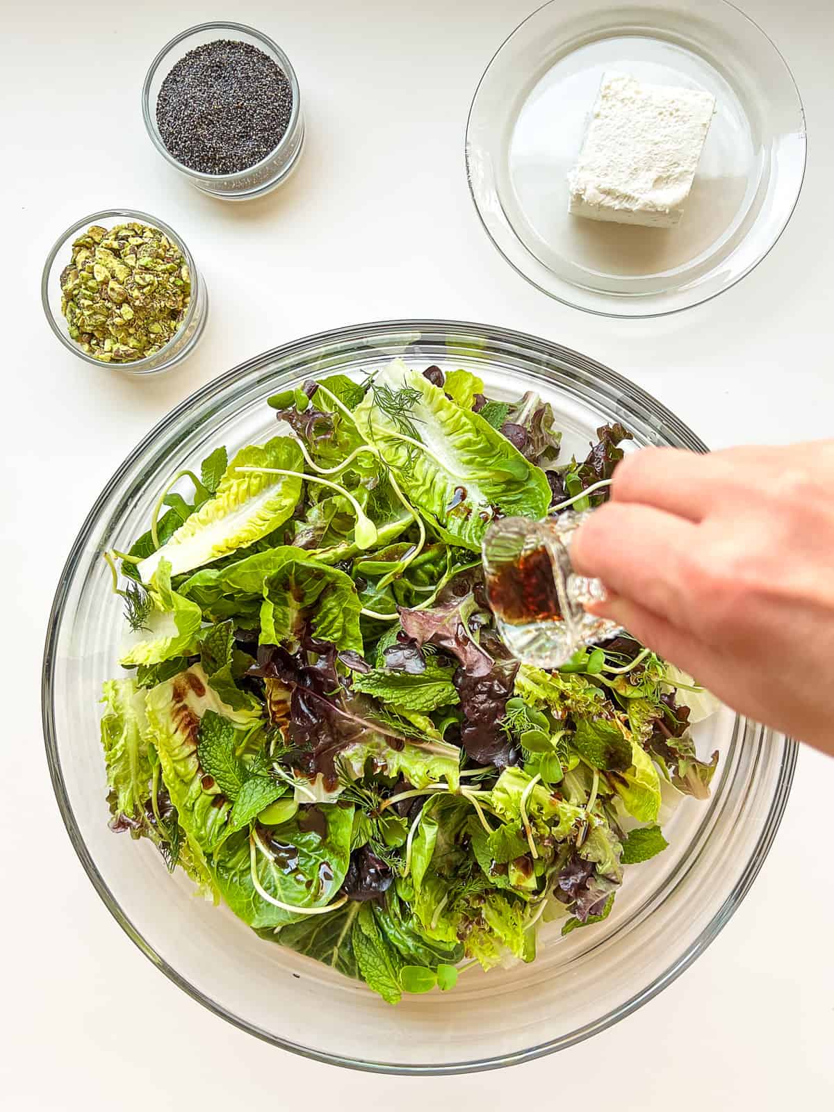 An image of a woman's hand pouring dressing over a salad.
