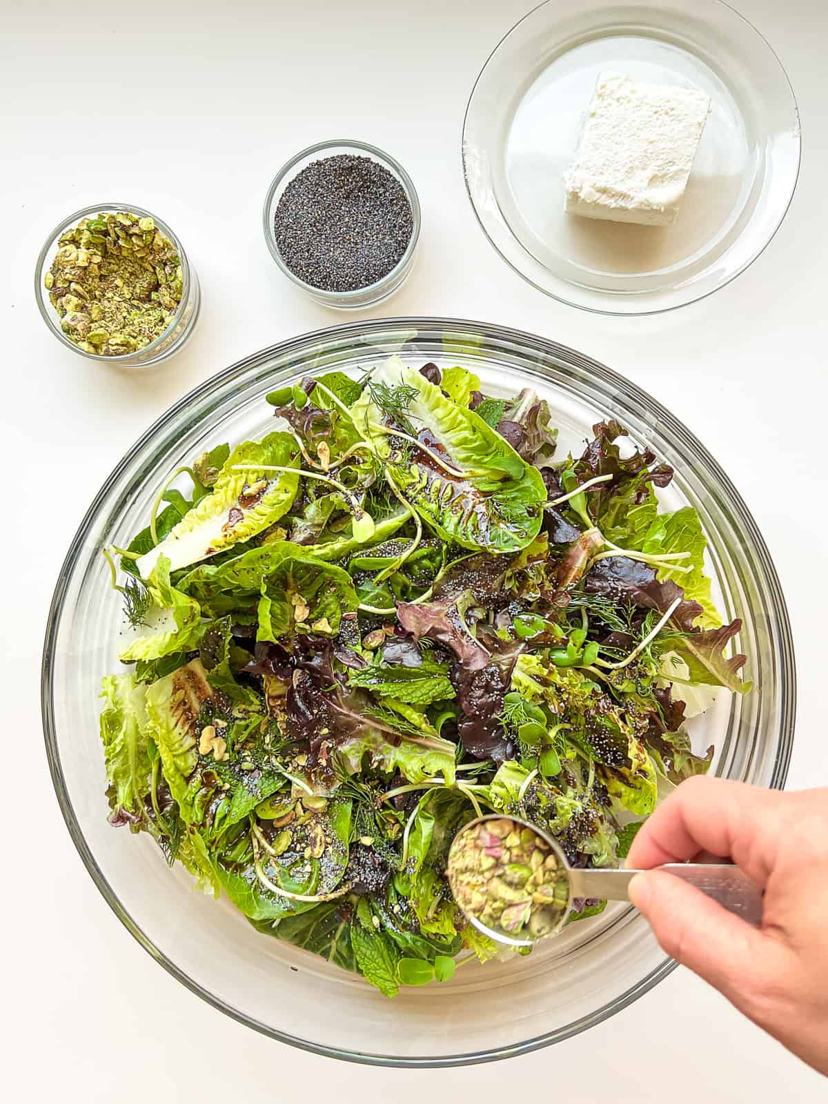 An image of a woman's hand sprinkling crushed pistachios over a salad.