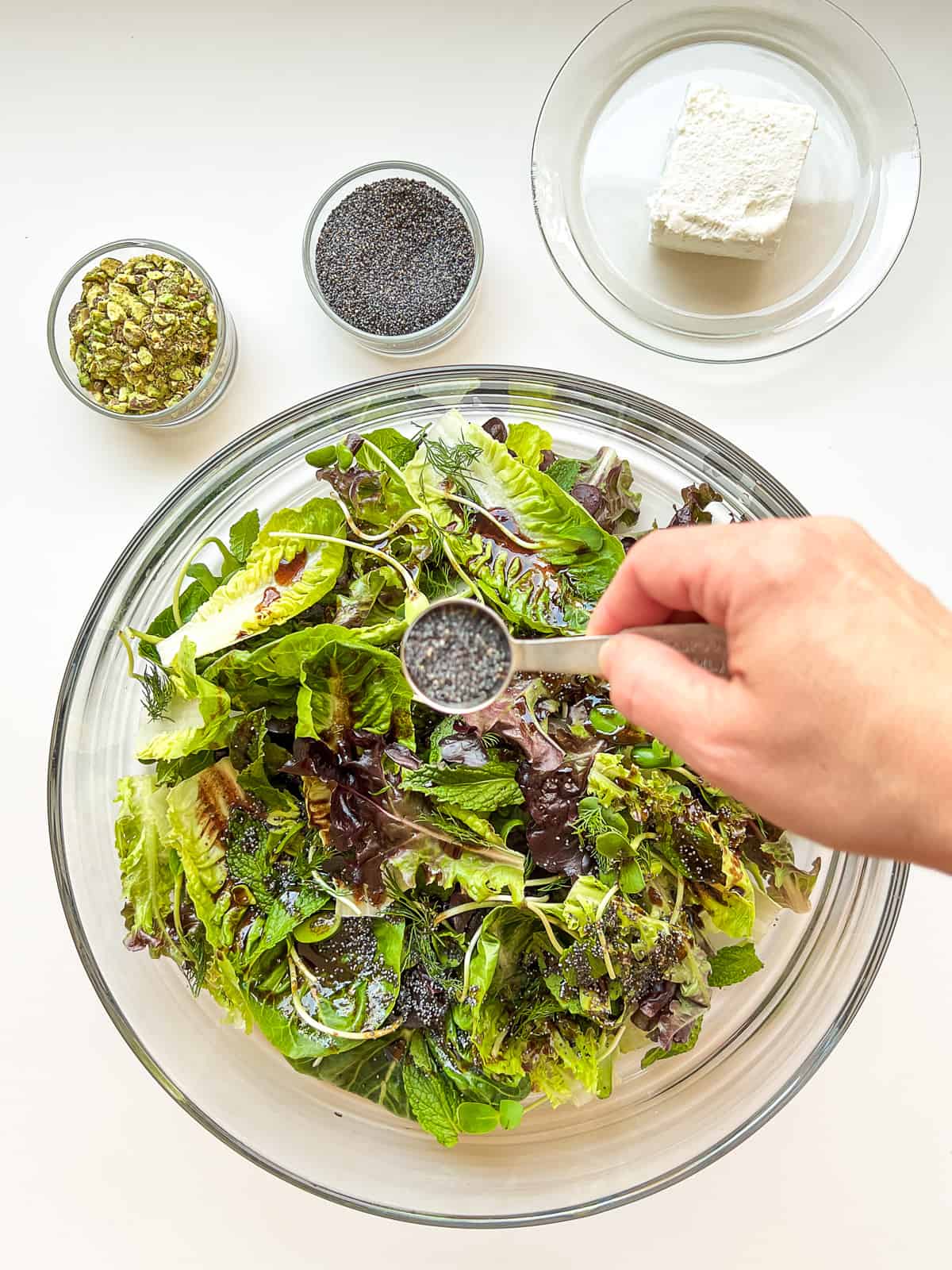 An image of a woman's hand sprinkling poppy seeds over a salad.