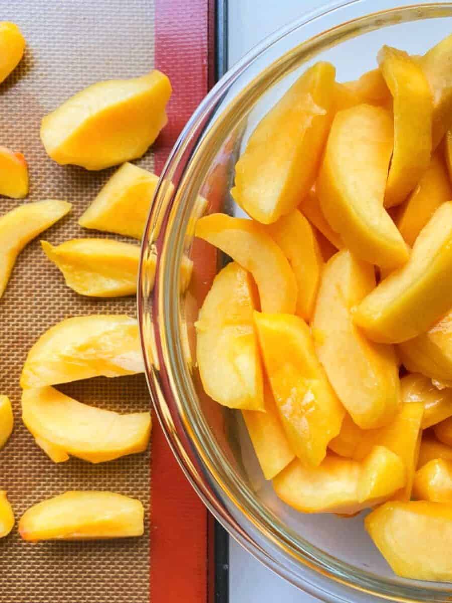 An image of peeled and cut peaches on a tray and in a bowl, ready to be frozen.