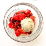 An image of Summer Fruit Salad in a glass bowl with a scoop of vanilla ice cream on top.