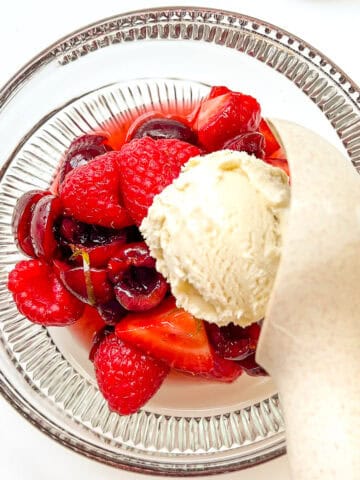 An image of Summer Fruit Salad in a glass bowl with a scoop of vanilla ice cream being scooped on top.