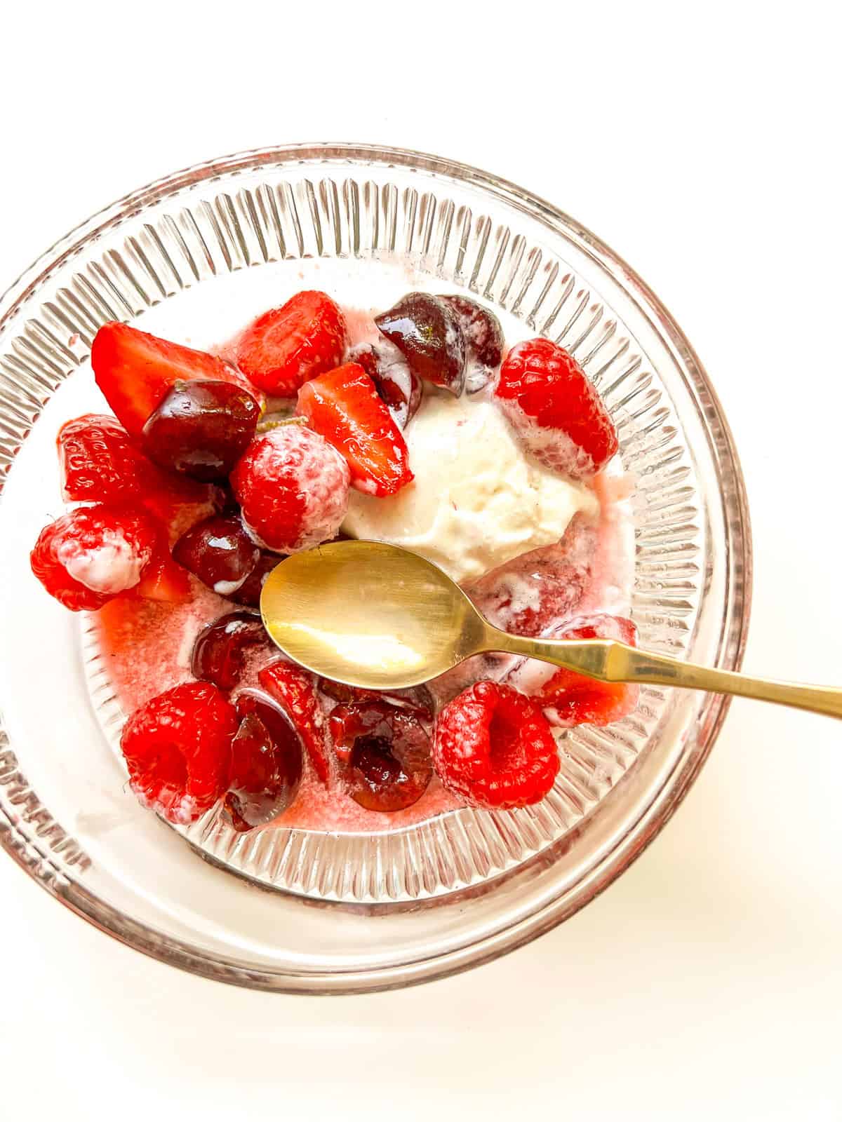 An image of Summer Fruit Salad and ice cream in a bowl with a brass spoon.