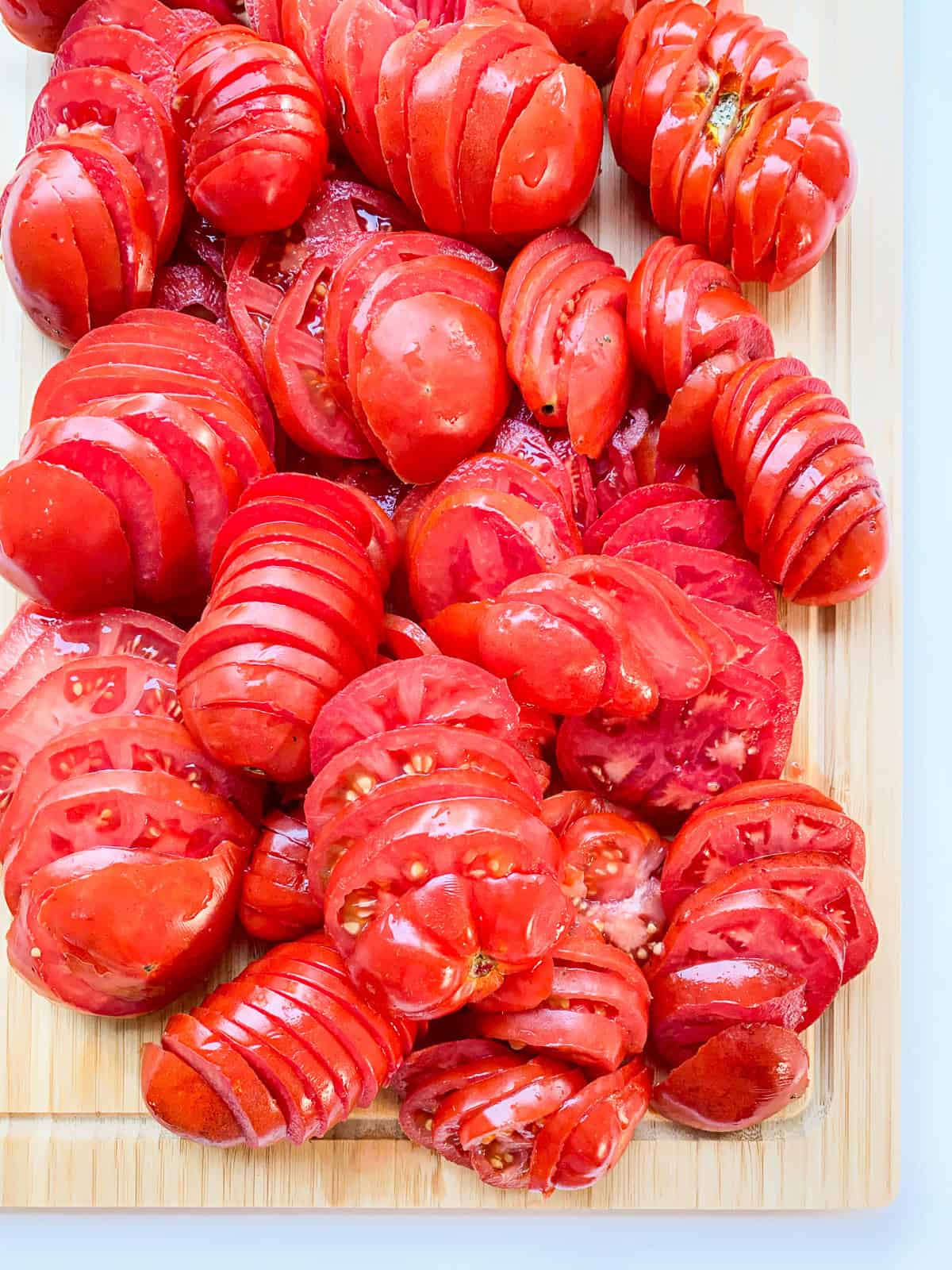 An image of a pile of cut tomato slices on a woode board.