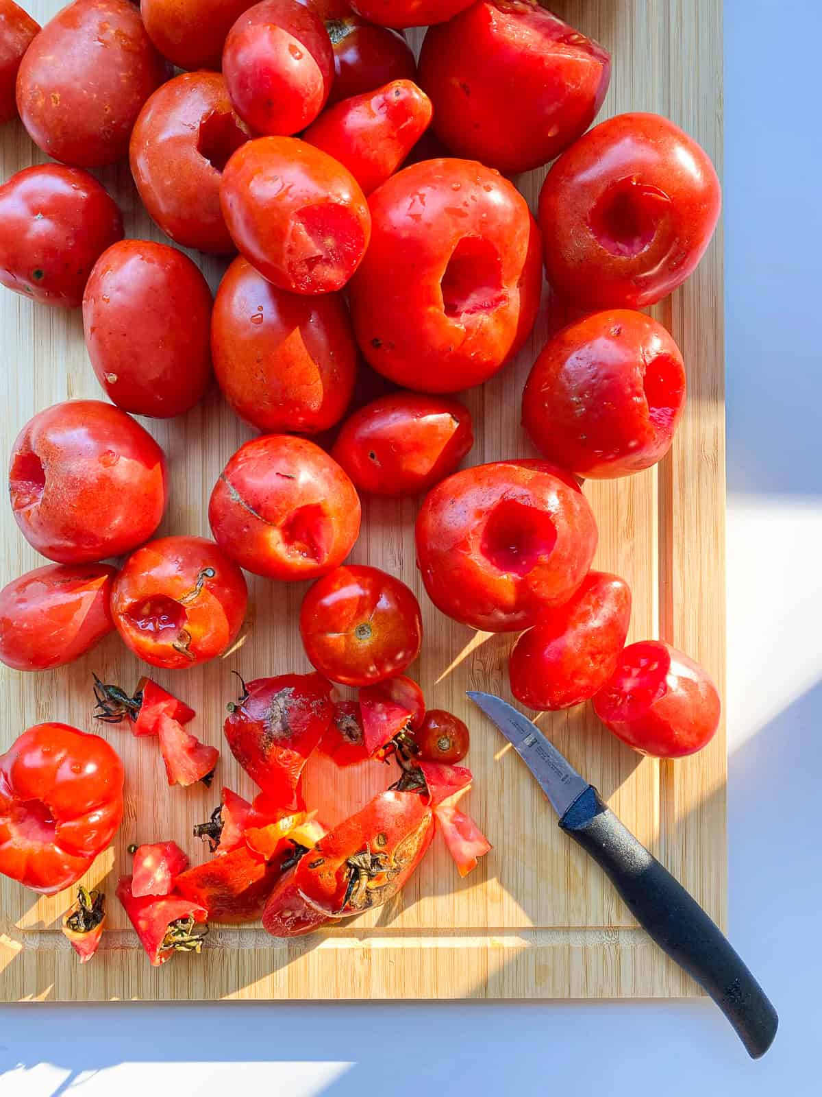 An image of tomatoes being cored on top of a wooden board.