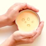 An image of two hands holding a small bowl of Corn and Miso soup against a light background.