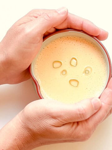 An image of two hands holding a small bowl of Corn and Miso soup against a light background.