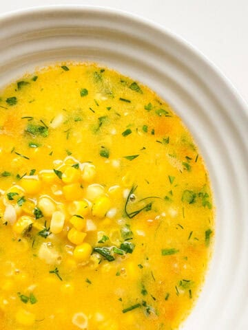 A white ceramic bowl of Corn Soup with Ginger and Dill.