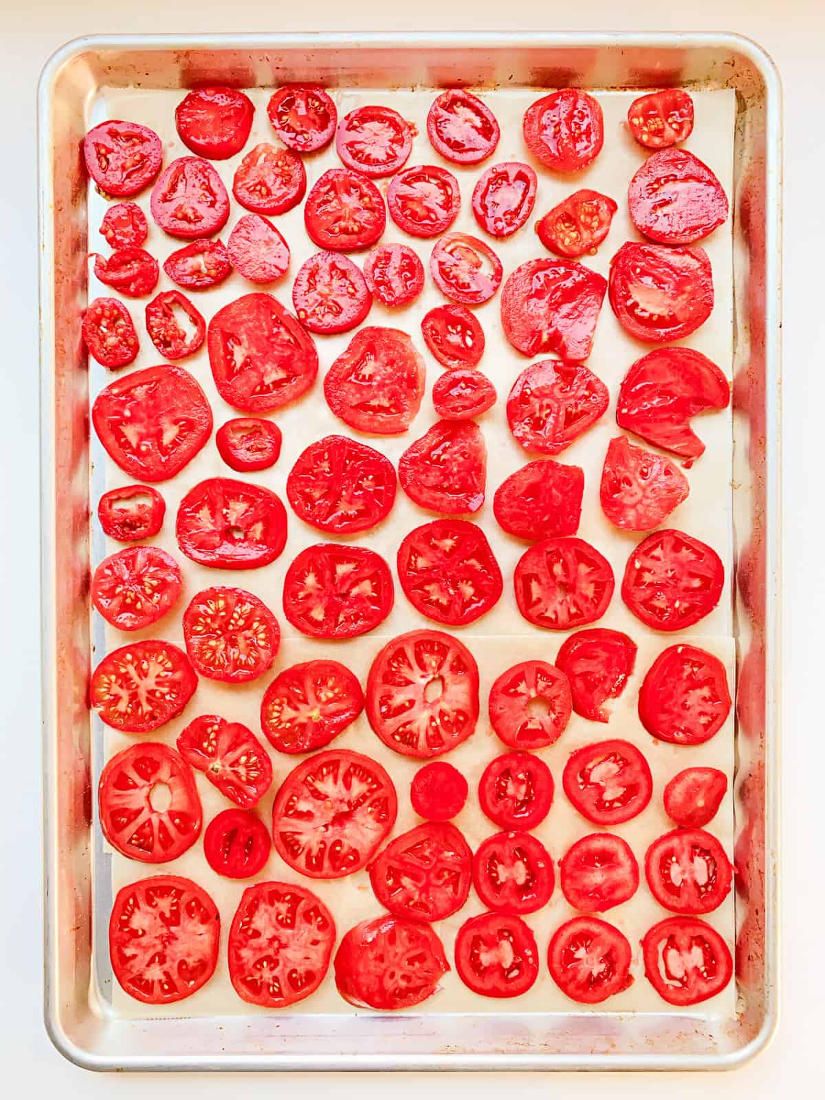 An image of cut tomato slices laid out on parchment paper on a baking tray.